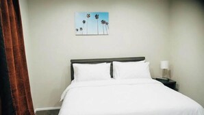 Habitación de hotel con cama, mesita de noche con lámpara y un cuadro de palmeras en la pared.