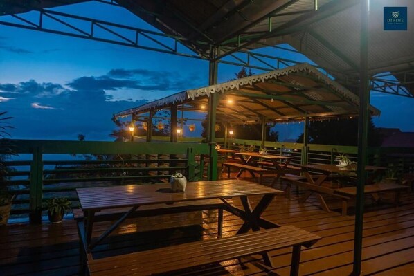 An outdoor dining area with wooden tables and benches, a covered seating area, and a view of the sky. - Divine Himalayan Resort (Darjeeling)