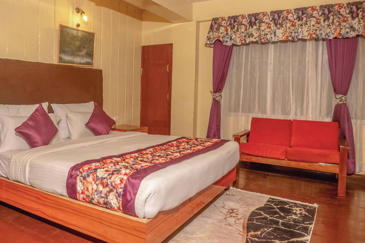 Una habitación de hotel con una cama de madera, un sofá rojo, una mesita de noche y una lámpara de pared.