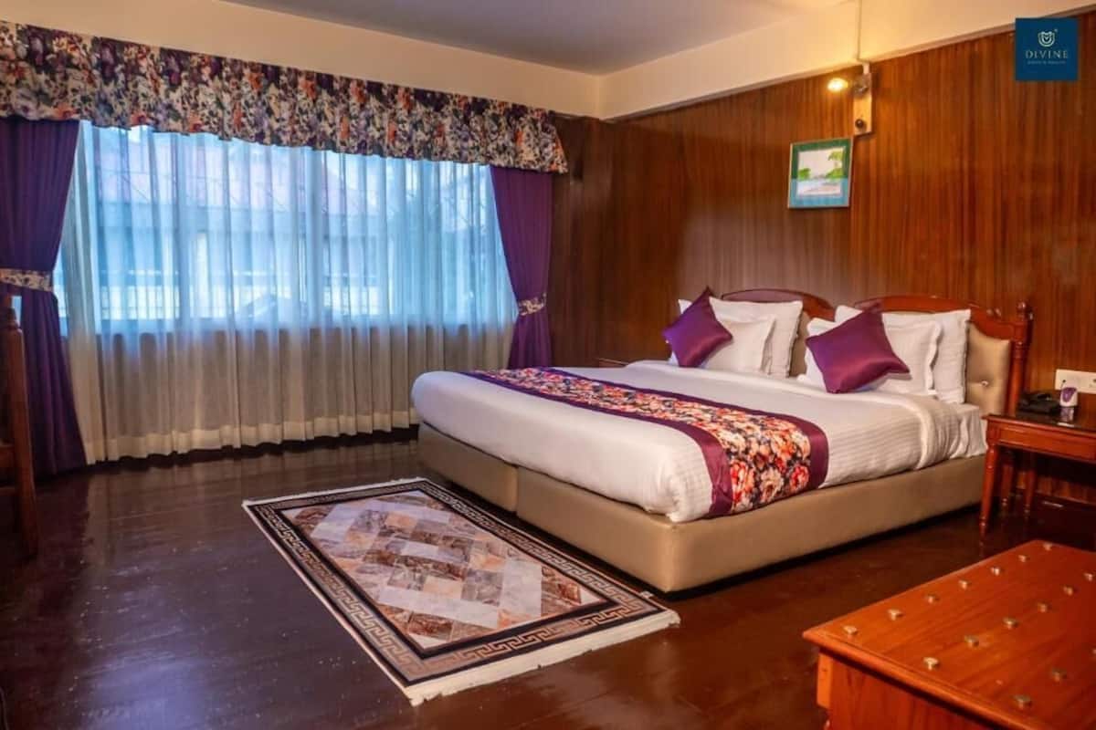 Habitación de hotel con una cama grande, suelo de madera, cortina con estampado floral y cabecero de madera.