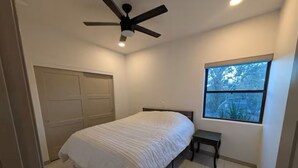 Et soveværelse med seng, ventilator, vindue og dør.