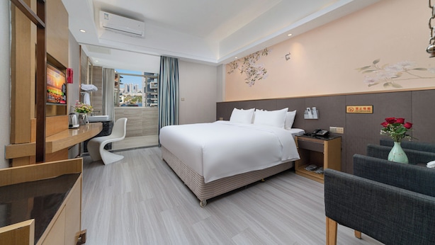 Une chambre d’hôtel comprenant un lit, un bureau, une chaise, une table de chevet et un vase avec des fleurs.