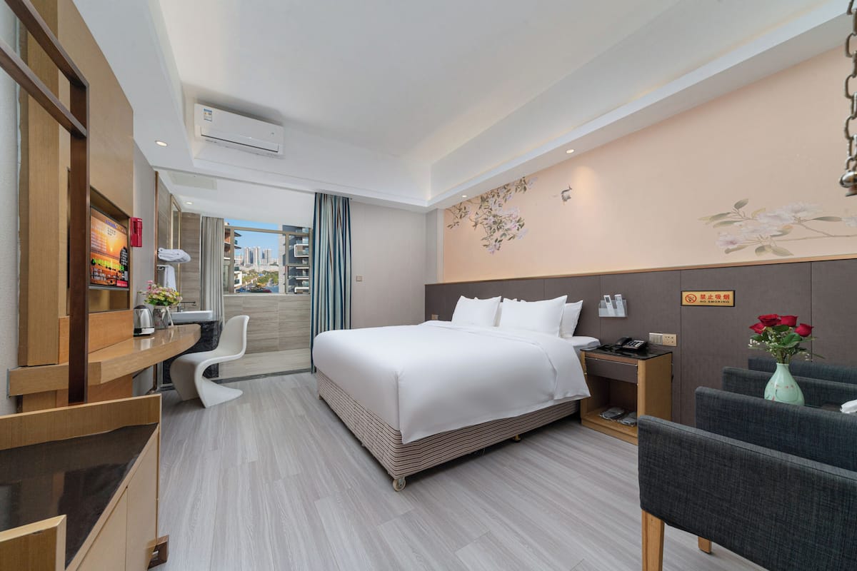 Ein Hotelzimmer mit Bett, Schreibtisch, Stuhl, Nachttisch und einer Vase mit Blumen.