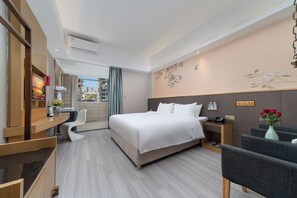 Una habitación de hotel con cama, escritorio, silla, mesita de noche y un florero con flores.
