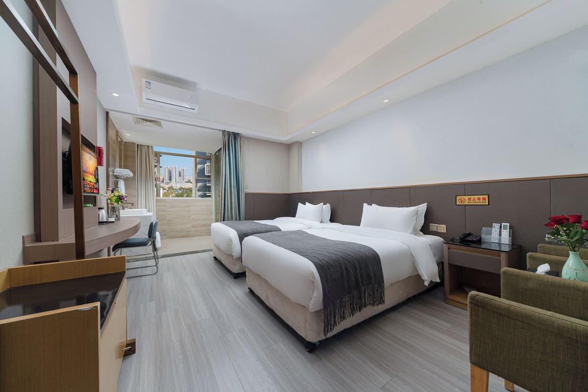 Ein Hotelzimmer mit einem großen Bett, einem Schreibtisch, einem Stuhl, einem kleinen Tisch und Blick auf die Stadt.