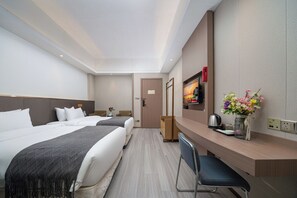 A hotel room with two beds, a desk, a chair, a TV, and a vase with flowers. - Weston Coastal Hotel Bao'an Intl Airport (Shenzhen)