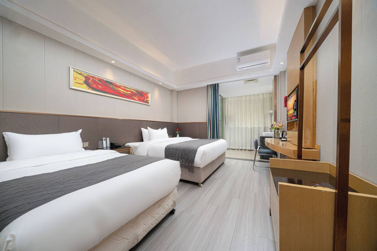 Ein Hotelzimmer mit zwei Betten, einem Schreibtisch, einem Sessel, einem Fernseher und einem Bild an der Wand.