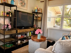 A living room with a television, shelves with various items, a window with blinds, and a sofa.
