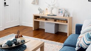 Ein Wohnzimmer mit Deckenventilator, Flachbildfernseher, Couchtisch aus Holz, blaues Sofa und weißer Tür.