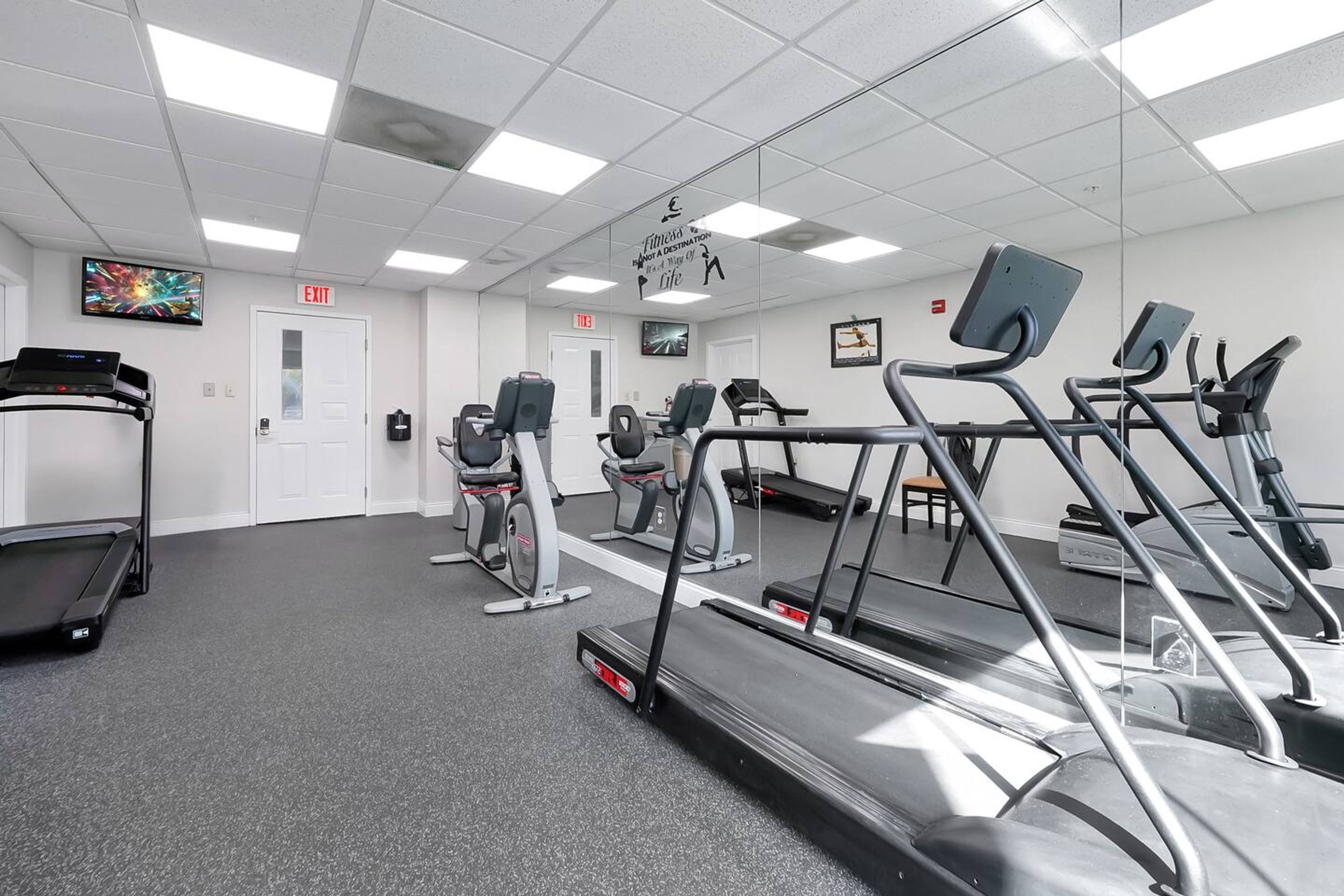 A gym with treadmills, elliptical machines, and a mirrored wall.