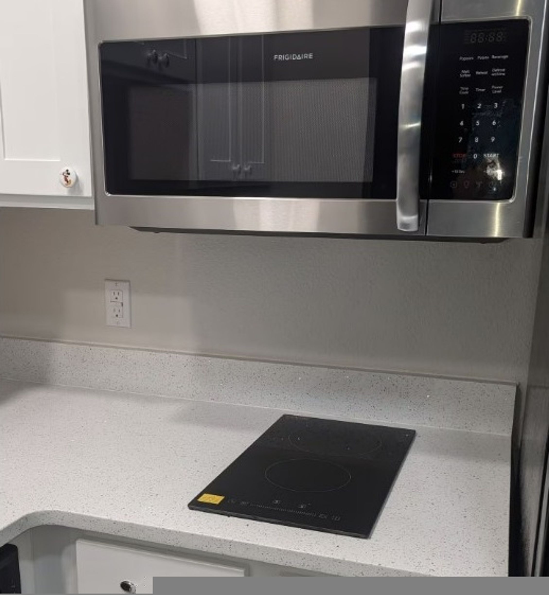 Une cuisine avec un four à micro-ondes en acier inoxydable placé au-dessus d’un plan de travail blanc.
