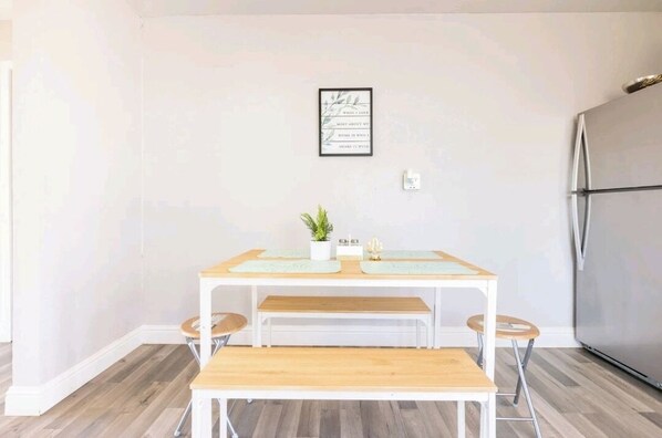 Una cocina con una mesa de madera, dos taburetes, un banco, un refrigerador y una cita enmarcada en la pared.