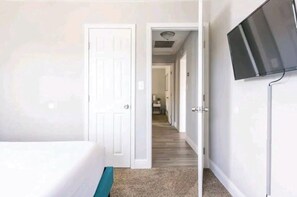 A bedroom with a bed, a television mounted on the wall, and a hallway leading to a bathroom.