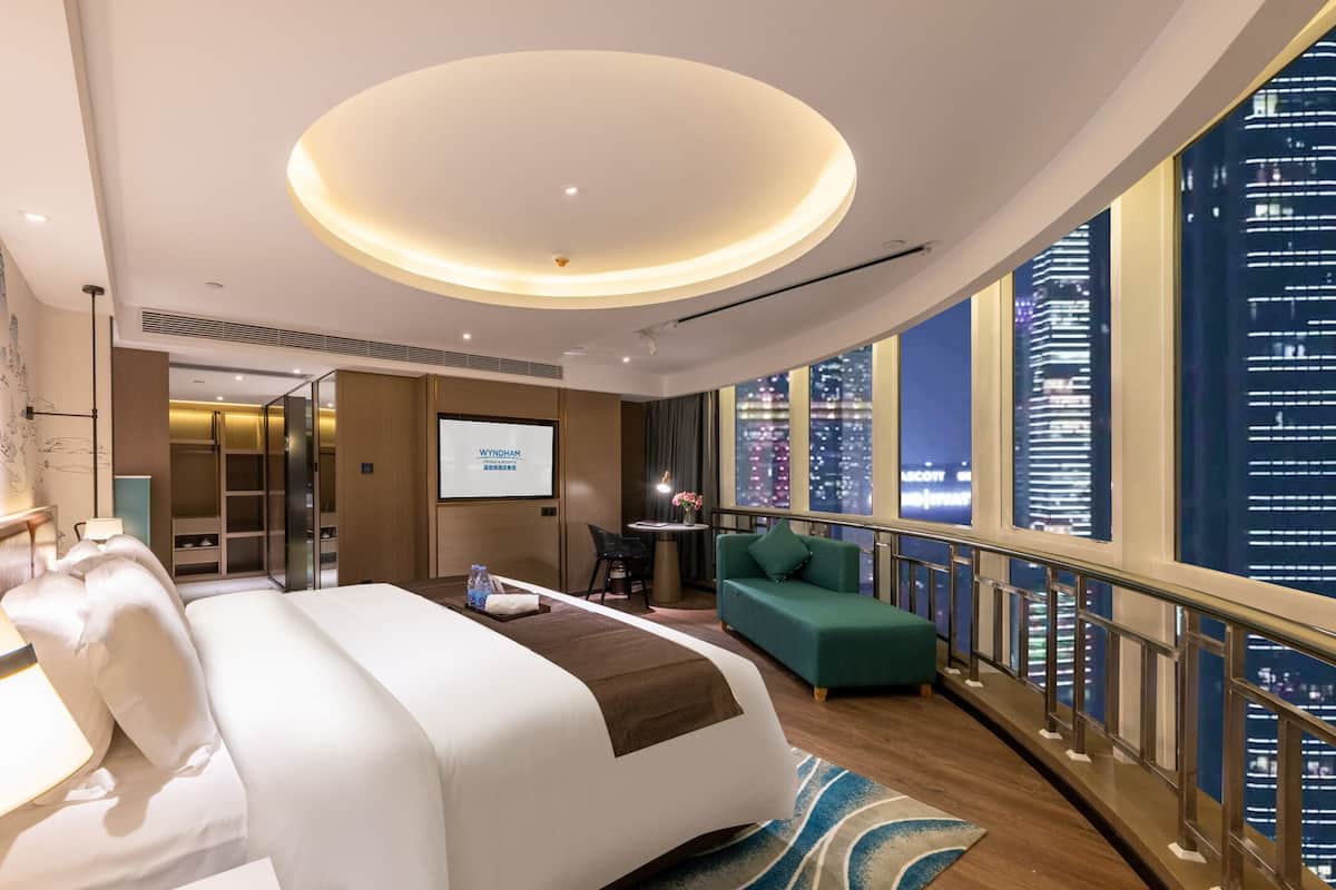 Ein modernes Hotelzimmer mit einem großen Bett, einer Sitzecke, einem Fernseher und Blick auf die Stadt.