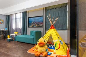 A hotel room with a large window, a television, a yellow duck plush toy, a play tent, and a teal sofa. - Ramada Encore International Hotel Jiangnanxi Metro Station Branch - Free Shuttle Bus to Canton Fair Complex During Canton Fair Period (Guangzhou)