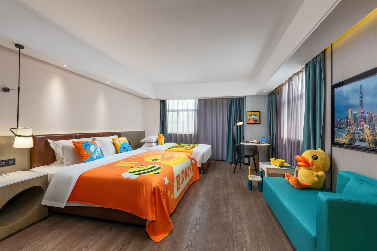 Ein Hotelzimmer mit zwei Betten, einem Sofa, einem kleinen Tisch und einem großen Fenster mit Vorhängen.