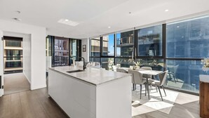 A modern kitchen with a central island, large windows, and a dining area with chairs. - Alfred Apartments by Arvia Living (Fortitude Valley)