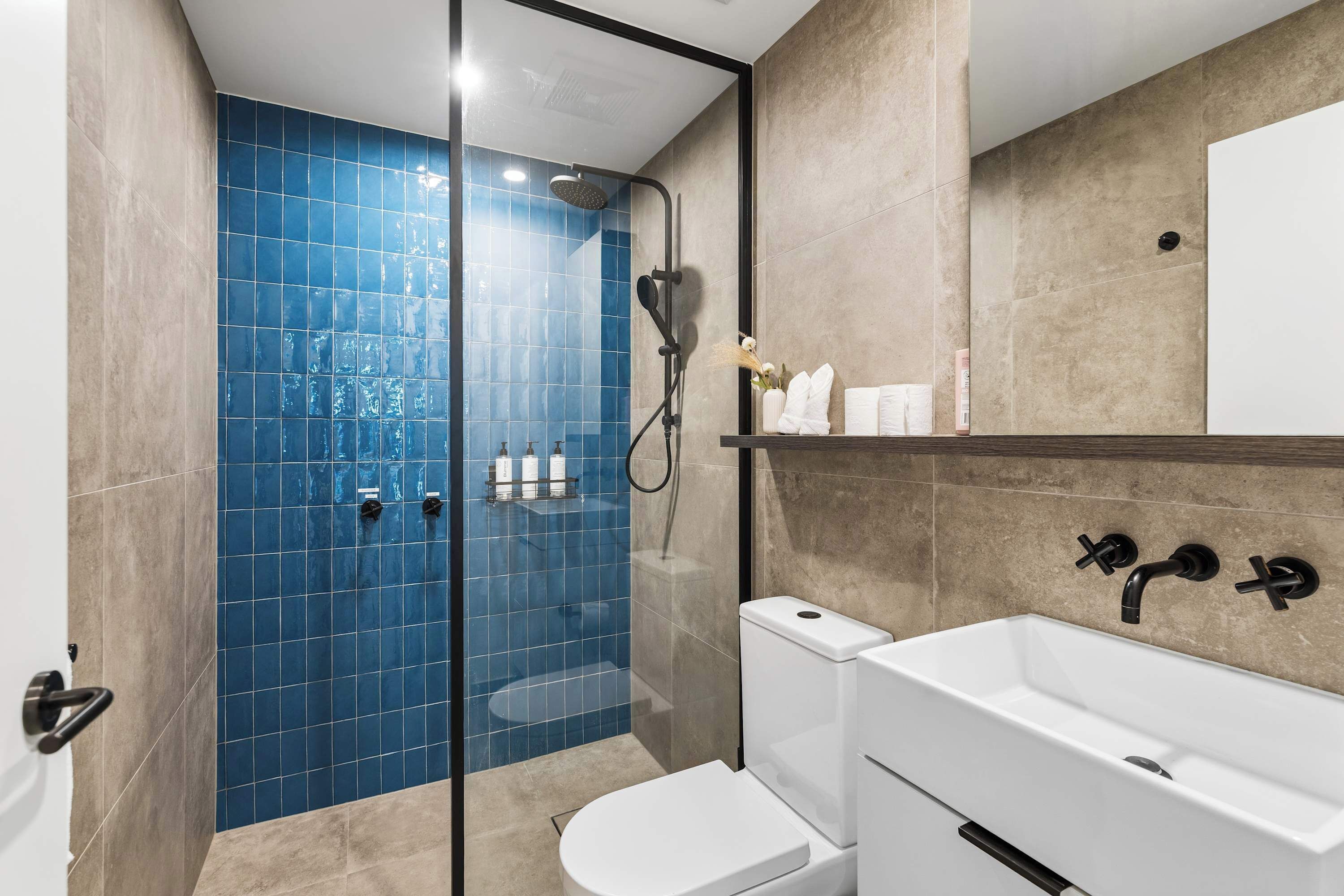 Casa de banho com cabine de chuveiro envidraçada, sanita branca e lavatório branco com acessórios pretos.