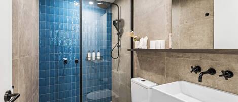 Casa de banho com cabine de chuveiro envidraçada, sanita branca e lavatório branco com acessórios pretos.