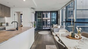 A modern kitchen with a central island, a dining area with a marble table, and a view through large windows. - Alfred Apartments by Arvia Living (Fortitude Valley)
