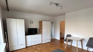 A modern, well-lit room with wooden flooring, a grey sofa, a small table with two chairs, and built-in wardrobes. - Perfect for City Break (Warsaw)