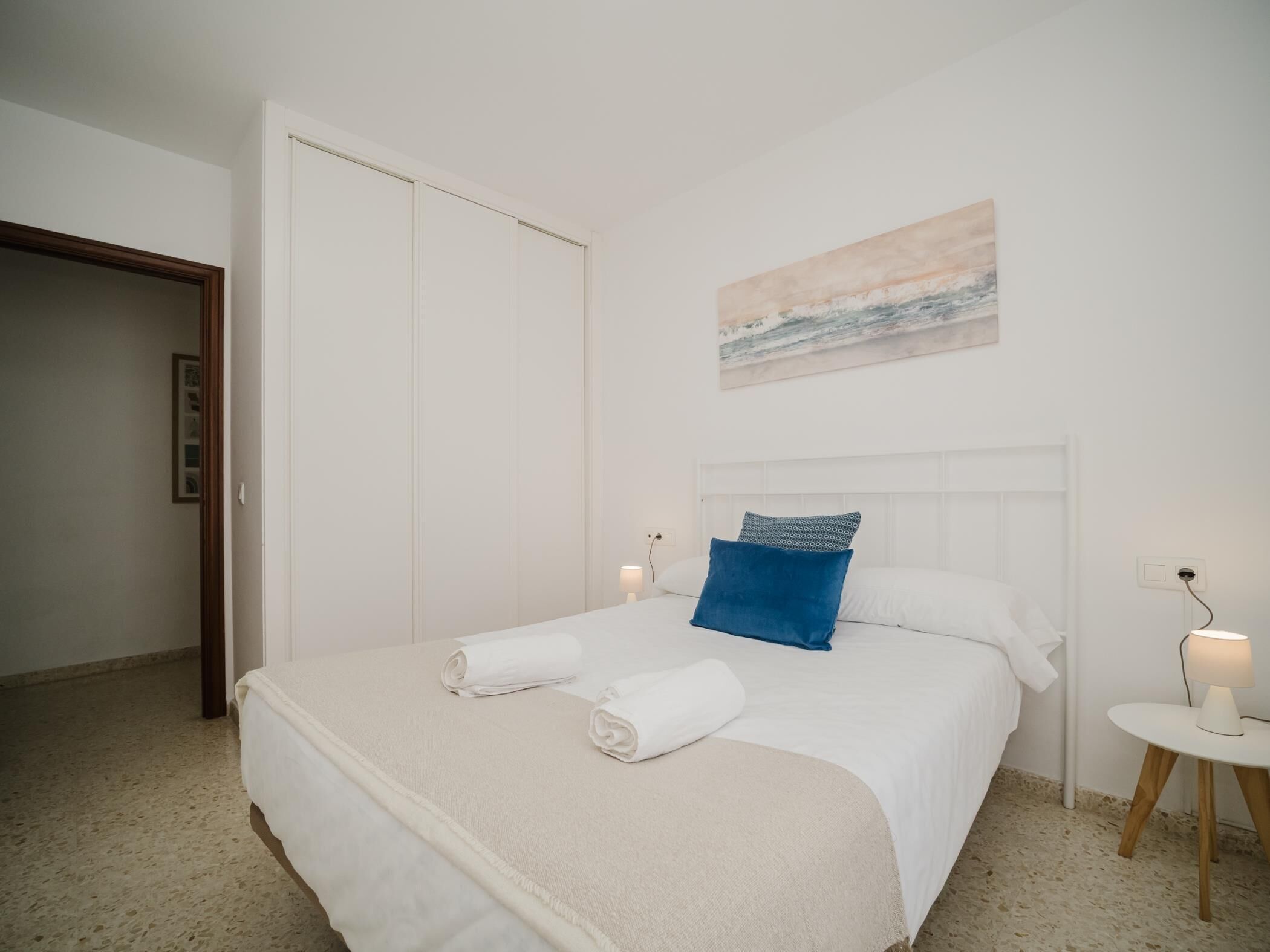Een hotelkamer met een bed, een nachtkastje, een aan de muur hangend schilderij en een deur.