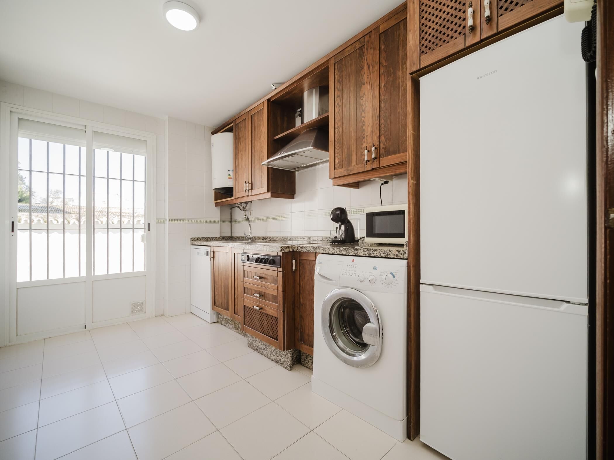 Une cuisine avec des meubles de rangement en bois, un lave-linge, un four à micro-ondes et un réfrigérateur.