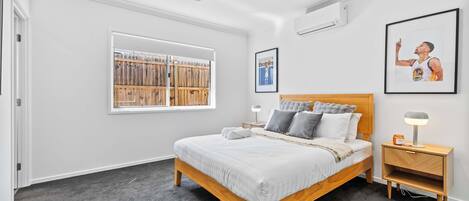 A bedroom with a bed, a nightstand, a ceiling fan, a window with blinds, and framed pictures on the wall.