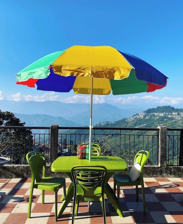 A table with a colorful umbrella, green chairs, and a view of mountains in the background.