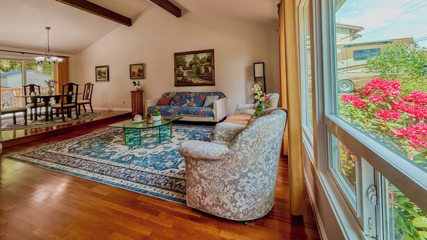 A living room with a sofa, a dining table with chairs, a coffee table, and a large window with a view of greenery and a vehicle. - Entire 3-bedroom charming house in Lake Forest Park (Lake Forest Park)