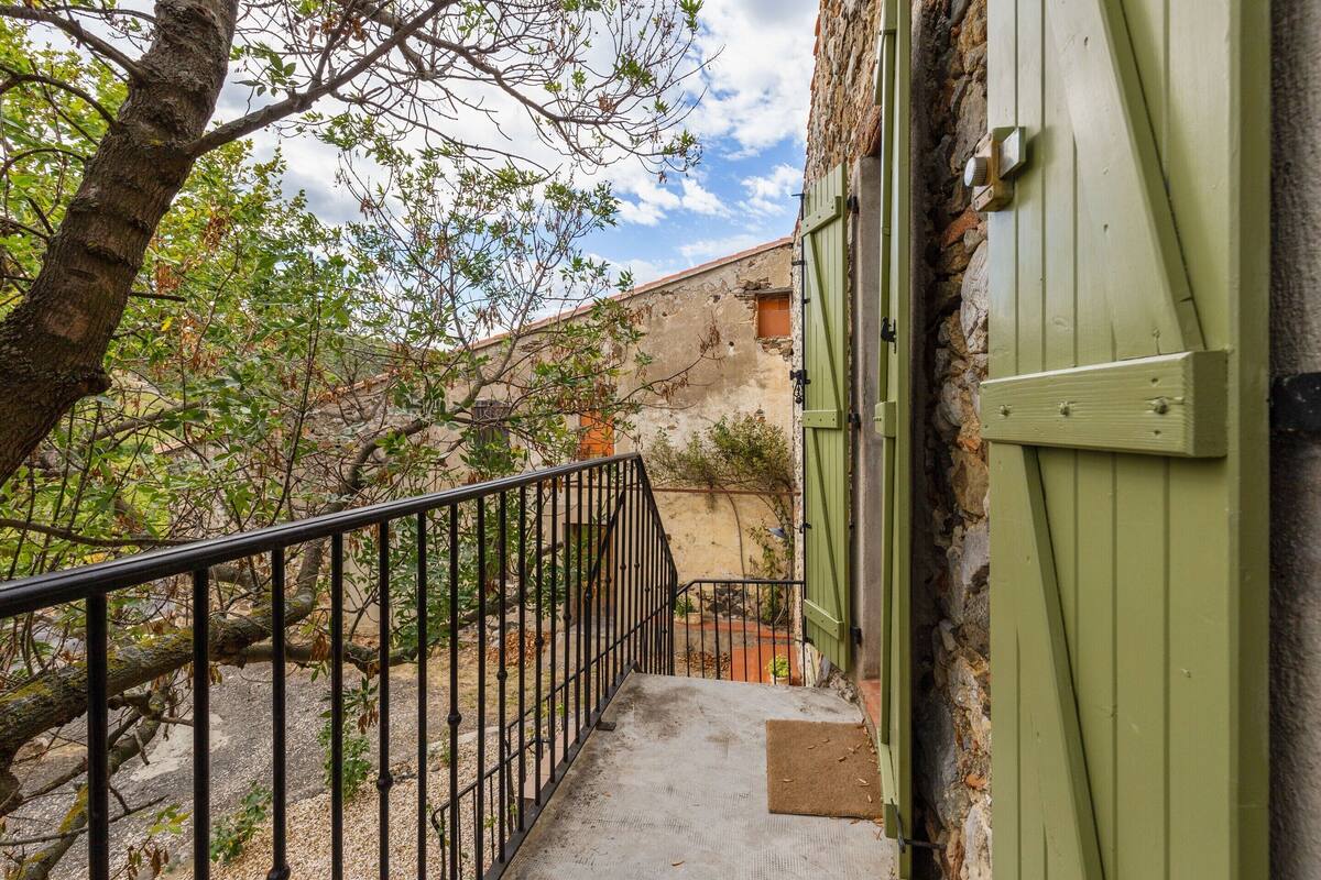 A narrow staircase leading to a green door, surrounded by a stone wall and a tree.