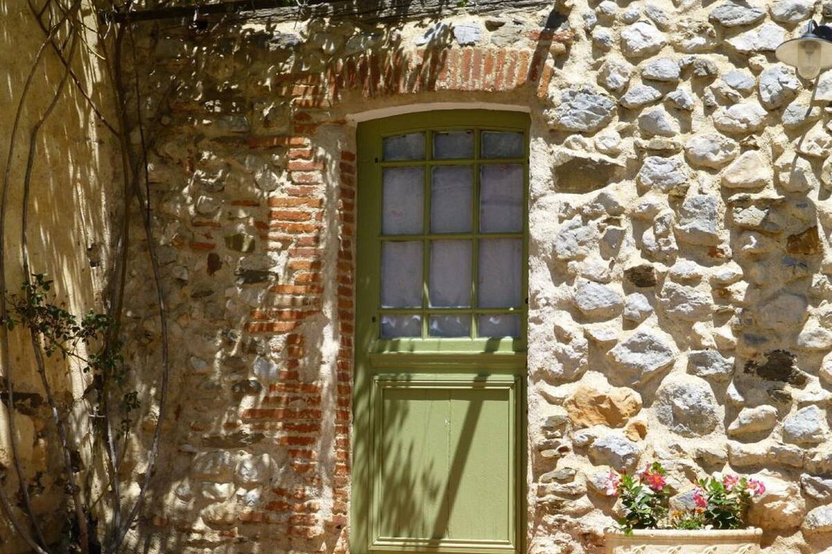 A stone building with a green door and a window, surrounded by vegetation.
