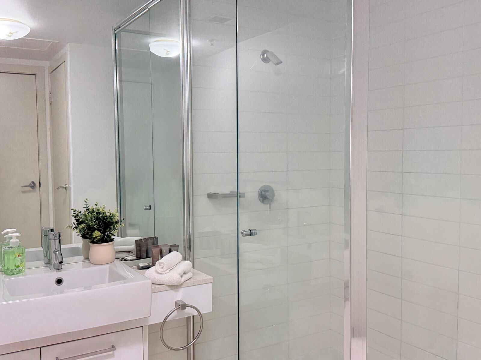 Un baño moderno con cabina de ducha de vidrio, un lavabo blanco con artículos de aseo y un espejo.