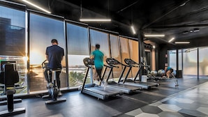 Une salle de sport moderne équipée de tapis de course, de ballons d’exercice et d’une grande fenêtre donnant sur la ville.