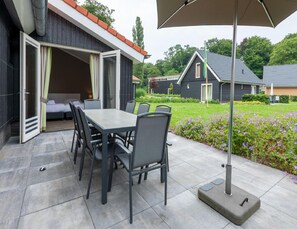 An outdoor patio with a table and chairs, a covered umbrella, and a view of neighboring houses and gardens. - Modern Villa With Garden (Almen)