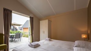 A hotel room with a large bed, a wardrobe, a dining area with chairs and an umbrella, and a view of the outside. - Modern Villa With Garden (Almen)