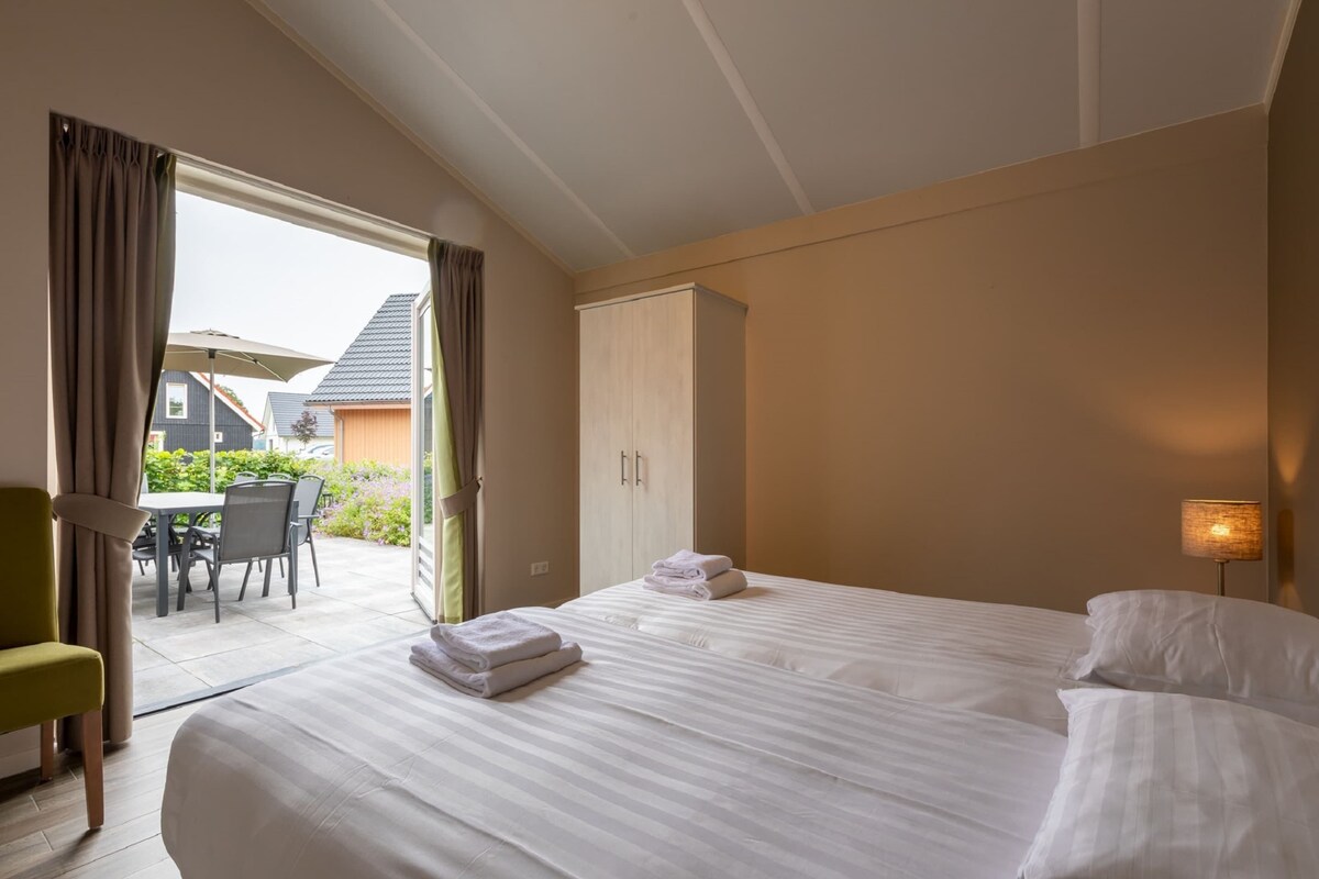 Une chambre d’hôtel avec un grand lit, une armoire, un coin repas avec des chaises et un parasol, et une vue sur l’extérieur.