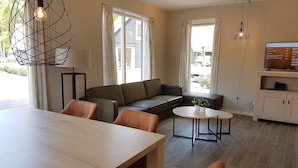 A modern living room with a wooden dining table, leather sofas, a small round table, and a TV on a wooden cabinet. - Modern Villa With Garden (Almen)
