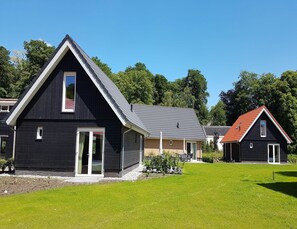 A row of modern houses with dark exteriors and sloped roofs, surrounded by a well-maintained lawn. - Modern Villa With Garden (Almen)