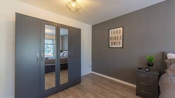A bedroom with a wardrobe, a bedside table with a plant, and a motivational quote on the wall.