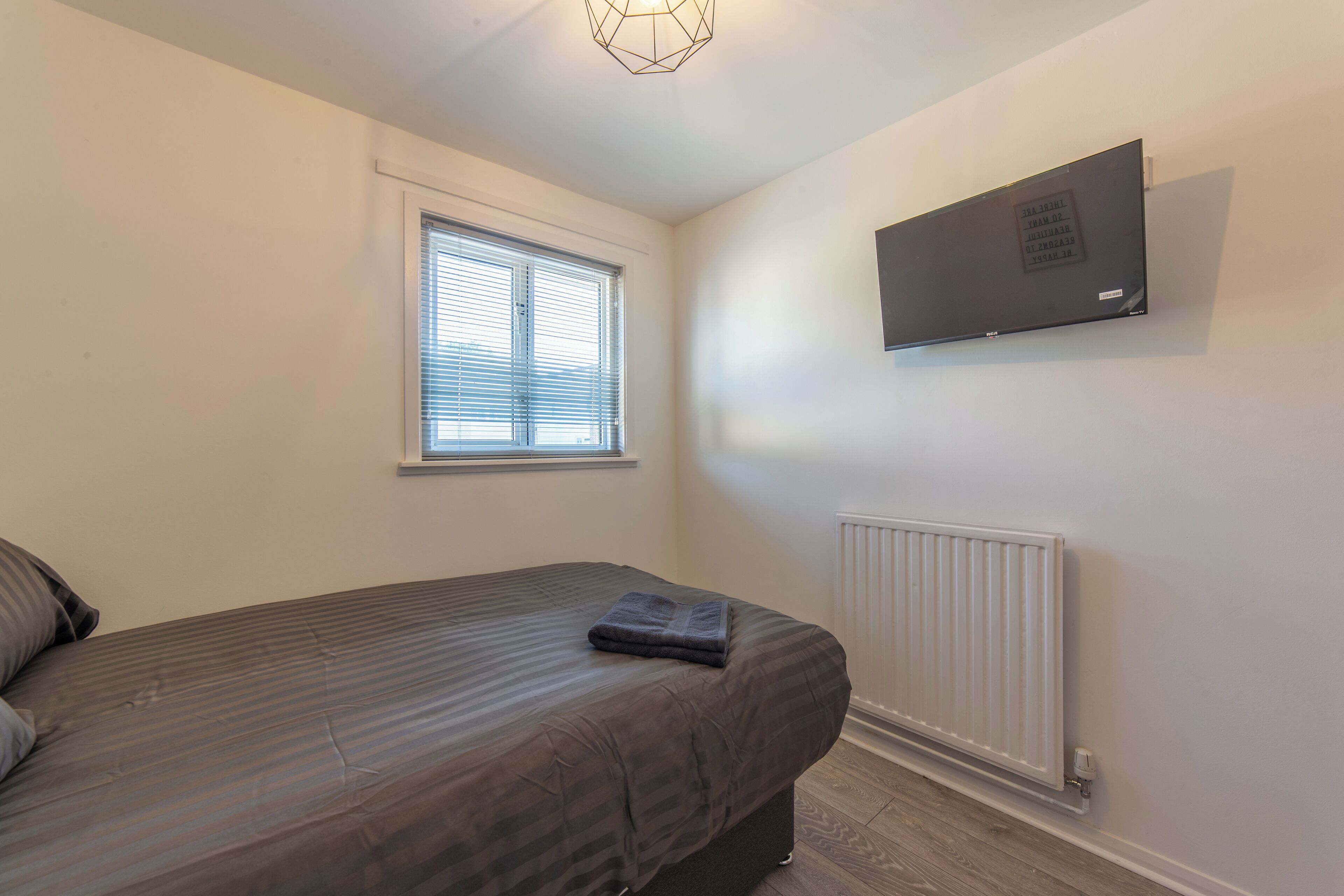 Ein Schlafzimmer mit einem Bett, einem Fenster, einem an der Wand befestigten Fernseher und einer Heizung.
