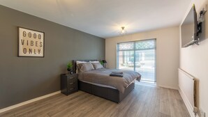 Un dormitorio moderno con cama, mesitas de noche, televisor en la pared y un ventanal grande.