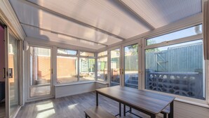 Un solárium con ventanas amplias, un banco de madera y una mesa.
