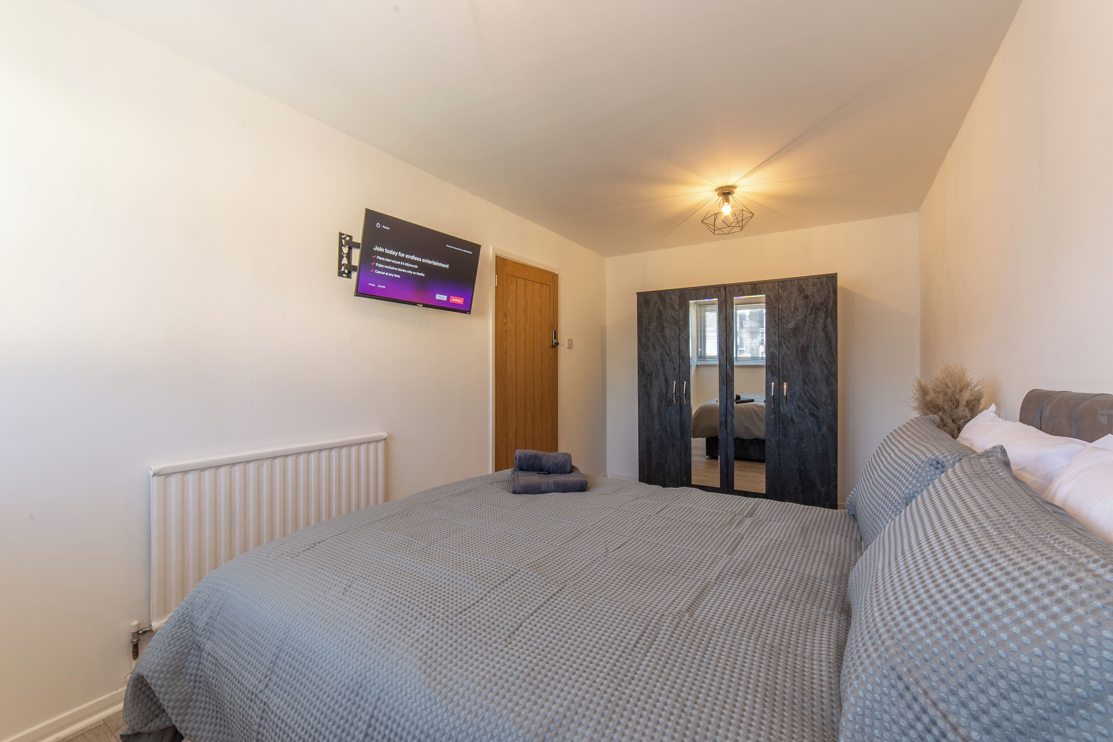 Ein Schlafzimmer mit Bett, Wandfernseher, Kleiderschrank und Heizkörper.