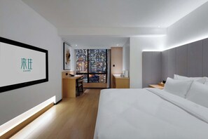 Ein modernes Hotelzimmer mit einem großen Bett, einem Schreibtisch und Blick auf eine Stadtlandschaft durch eine Glaswand.