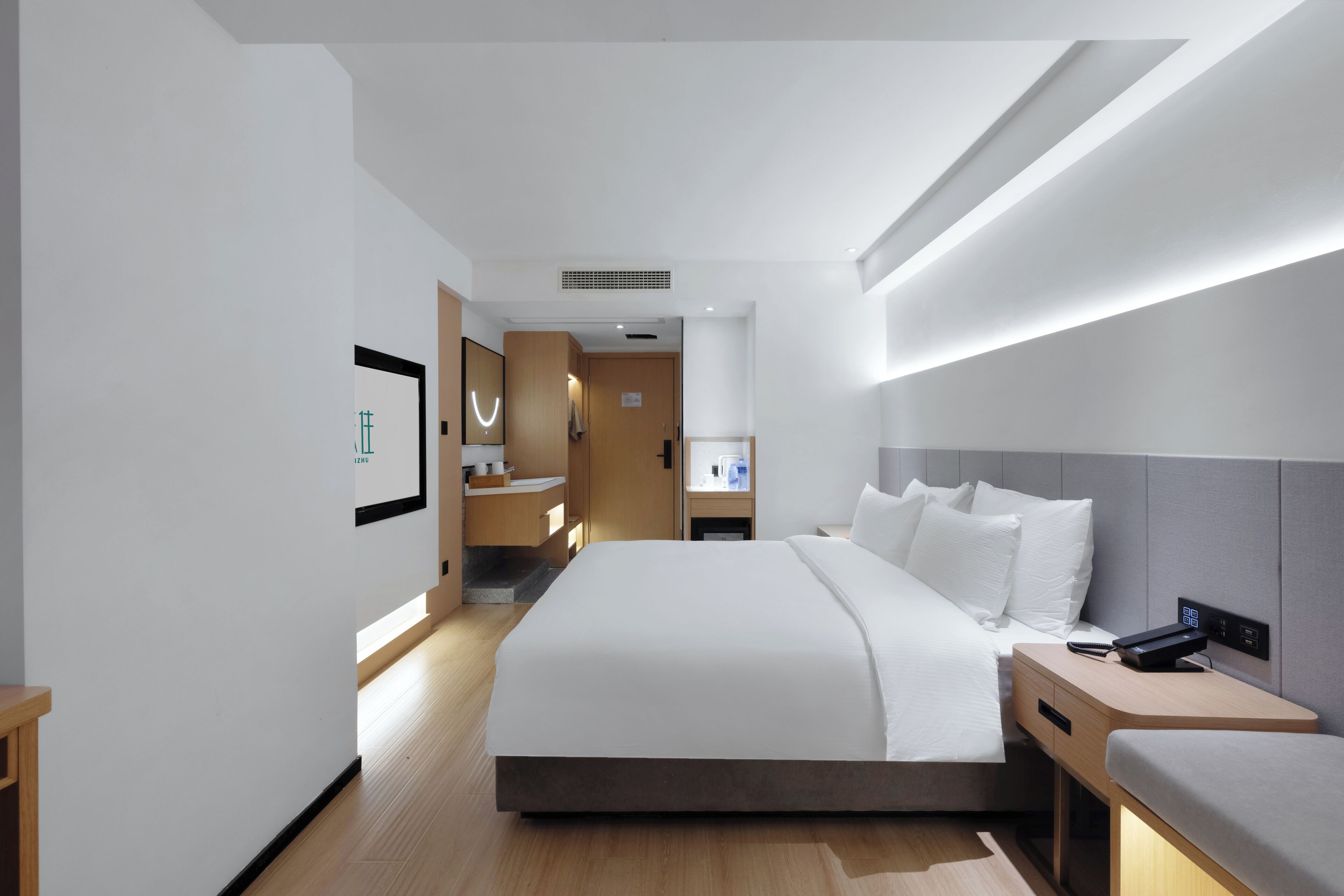 Ein modernes Hotelzimmer mit einem großen Bett, Nachttischen, einem Beistelltisch und einem durchgegangenen Tür sichtbaren Badezimmer.