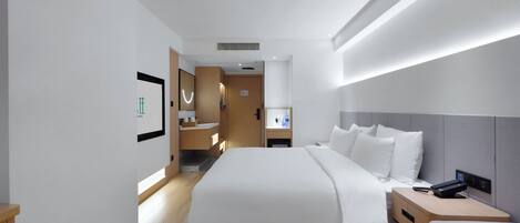Ein modernes Hotelzimmer mit einem großen Bett, Nachttischen, einem Beistelltisch und einem durchgegangenen Tür sichtbaren Badezimmer.