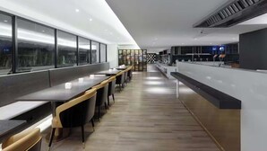 Egy modern étterem, ahol hosszú asztalok, fa padló és nagy ablakokon át nyíló kilátás várja a vendégeket.