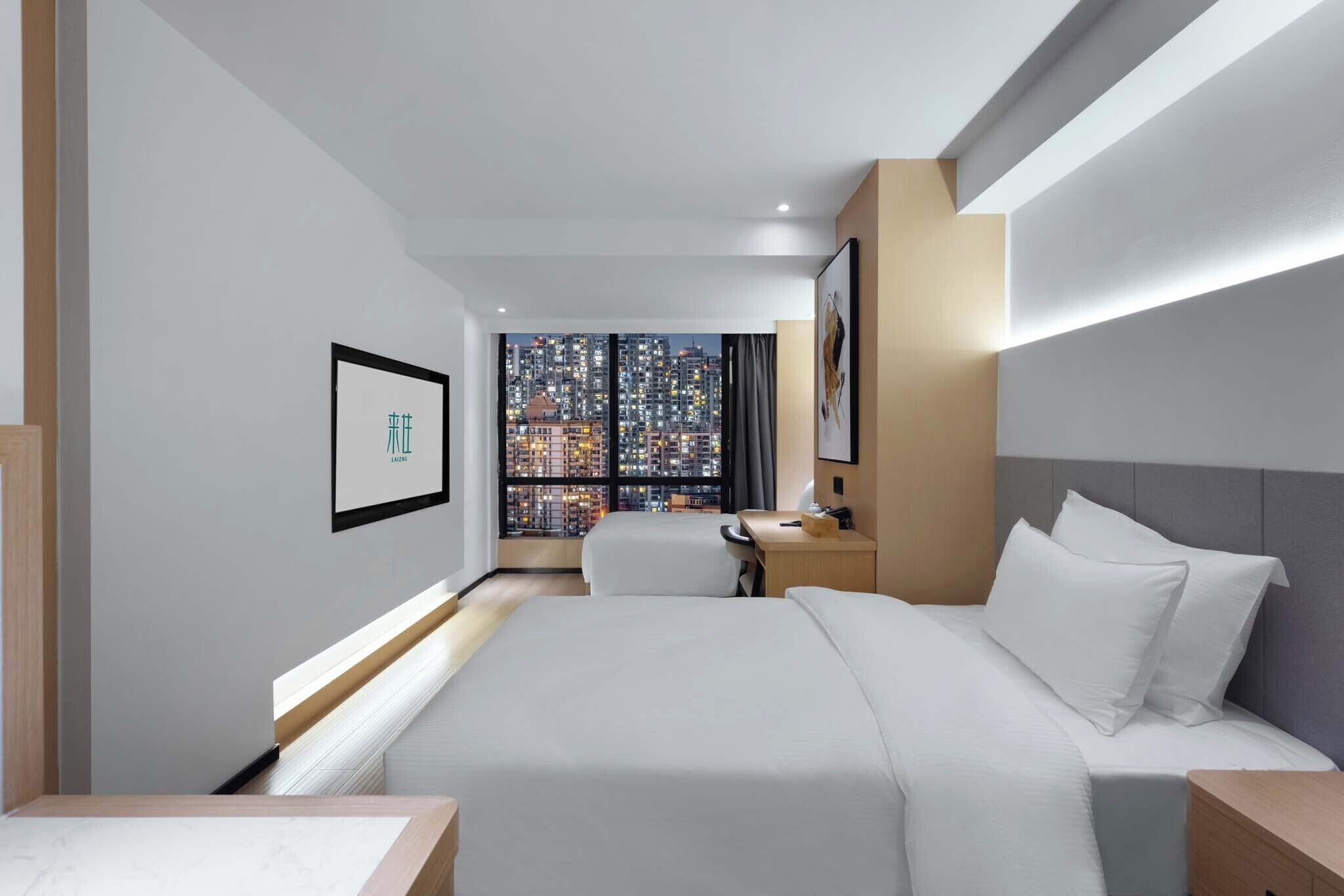 Habitación de hotel moderna con una cama grande, un escritorio y vistas a un paisaje urbano a través de amplios ventanales.