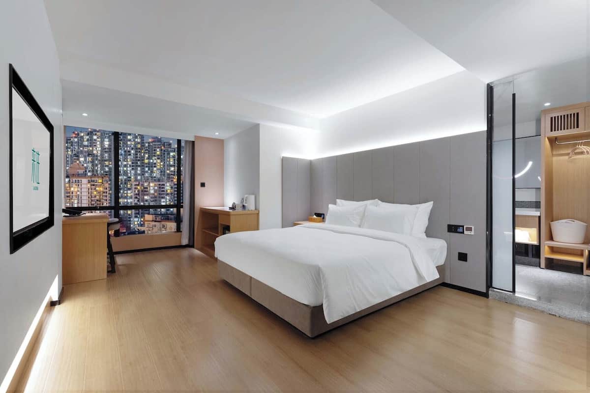 A modern hotel room with a large bed, a nightstand, a desk, and a wardrobe.
